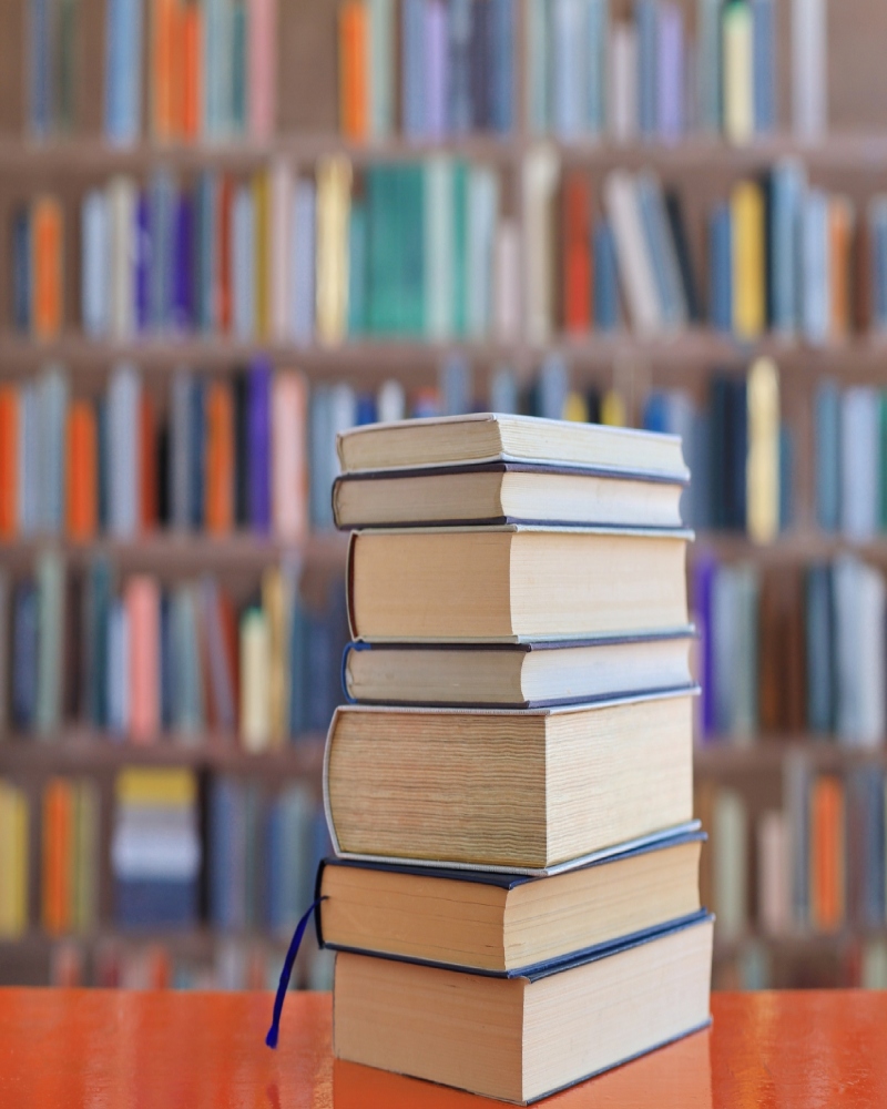 Bücherstapel in Bibliothek, Bücherwand aus dem Fokus im Hintergrund
